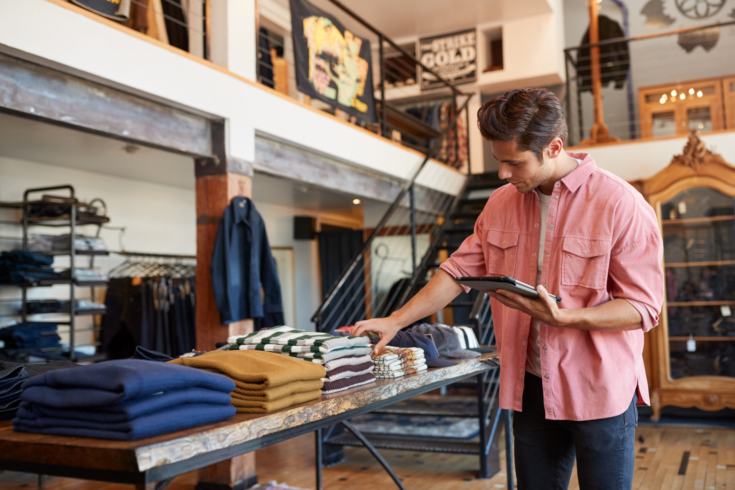Male Owner Of Fashion Store Using Digital Tablet To Check Stock In Clothing Store