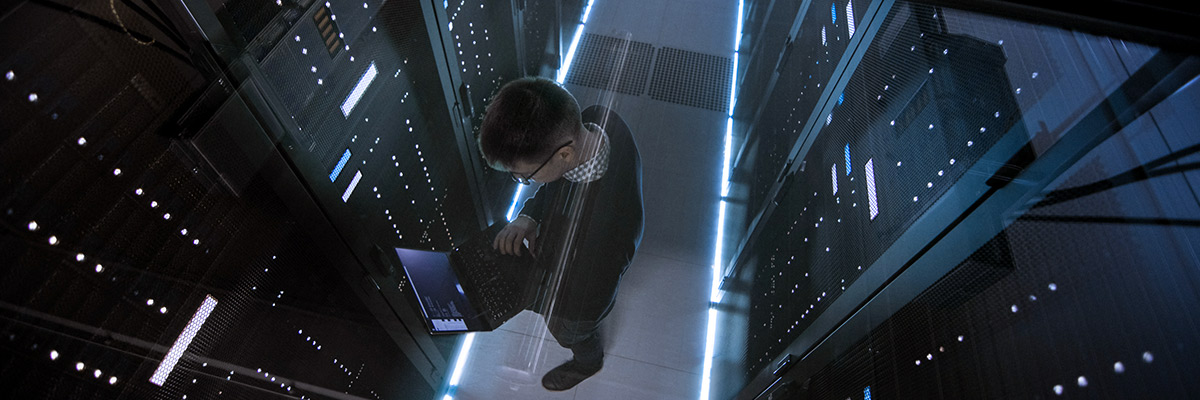 tall man working on his laptop in a server room