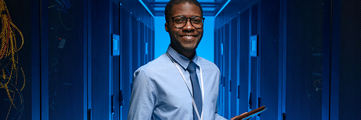 man happily working in a server room on his tablet